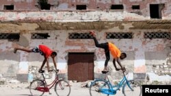 Somali boys perform tricks on their bicycles near a ruined building in Hamarweyne district of Mogadishu, Jan. 25, 2021. With poor roads and equipment, Somalia's cycling federation faces an uphill battle to prepare for upcoming international competition.