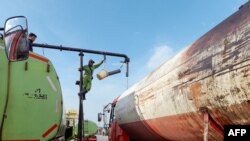 Para petugas memindahkan minyak sawit mentah ke truk tangki di pelabuhan Tanjung Emas Semarang, sebelum didistribusikan ke pabrik pengemasan minyak goreng, 7 April 2022. (Daffa Ramya KANZUDDIN / AFP)