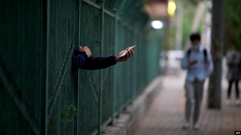 一名居民从北京潘家园因新冠疫情被封控的小区栅栏里伸出握着手机的手。（2022年4月27日）(photo:VOA)