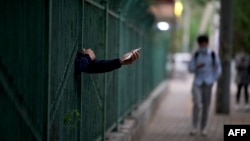 一名居民从北京潘家园因新冠疫情被封控的小区栅栏里伸出握着手机的手。（2022年4月27日）