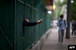 一名居民从北京潘家园一个封控小区的栅栏里伸出握着手机的手。（2022年4月27日）