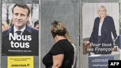 Une femme passe devant des affiches de campagne du président français Emmanuel Macron et de son adversaire Marine Le Pen, à Eguisheim, en France.