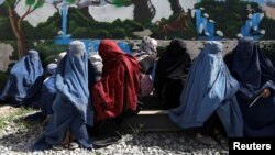 FILE - Afghan women wait to receive food packages being handed out at a humanitarian aid distribution center in Kabul, Afghanistan, April 25, 2022.