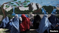 FILE - Afghan women wait to receive a food package being distributed by a Saudi Arabia humanitarian aid group at a distribution center in Kabul, Afghanistan, April 25, 2022.