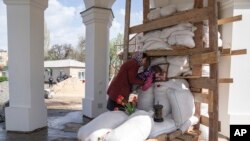 Seorang penganut Ortodoks membantu putrinya mencium foto seorang pendeta, pendiri gereja All Saints pada perayaan Paskah di Bahmut, Ukraina timur, Minggu, 24 April 2022. (AP/Evgeniy Maloletka)