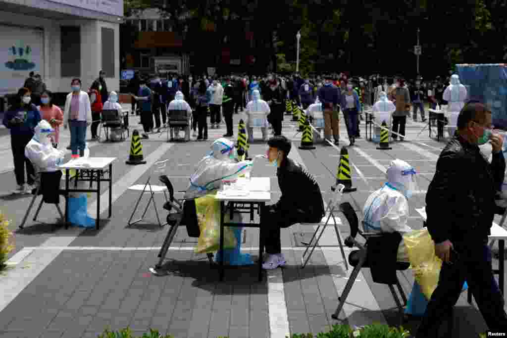 A medical worker in protective clothes collects a sample from a local person at a temporary testing center during the COVID-19 outbreak in Beijing, China.