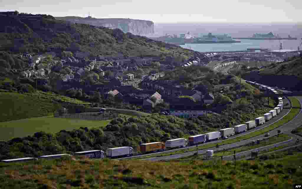 Freight lorries and HGVs (heavy goods vehicles) queue on the A20 road towards the Port of Dover, as the P&amp;O ferry &#39;Spirit of Canterbury&#39; (R) is pictured moored to the quayside at the port, on the south-east coast of England.