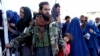 FILE - A Taliban fighter stands guard as people receive food rations distributed by a Saudi humanitarian aid group, in Kabul, Afghanistan, April 25, 2022. 
