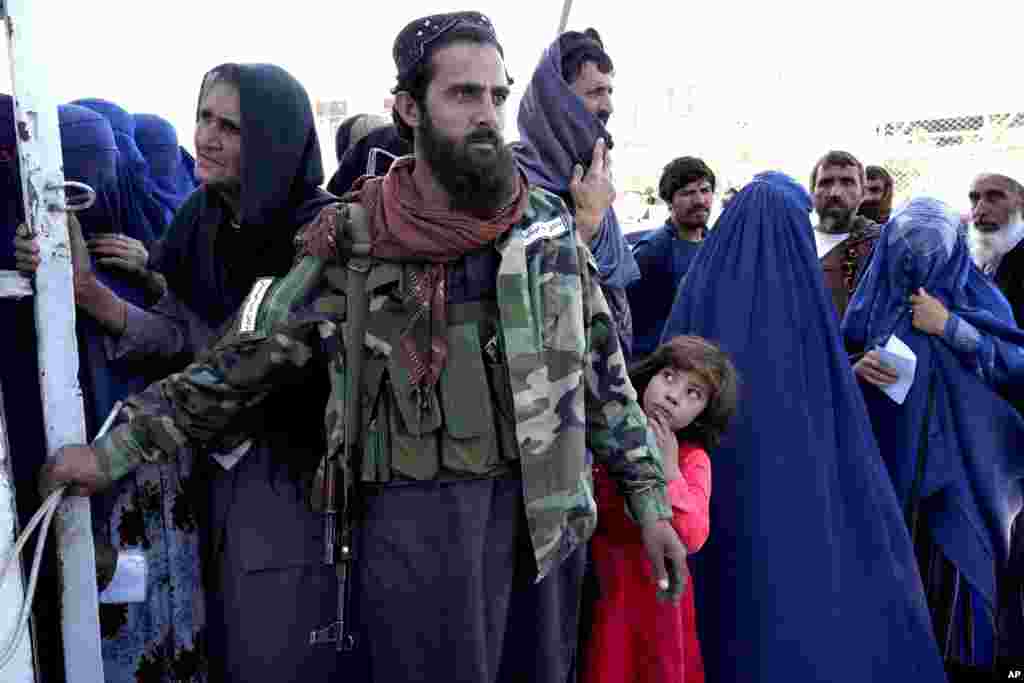 A Taliban fighter stands guard as people receive food given out by a Saudi humanitarian aid group, in Kabul, Afghanistan.