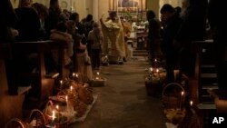 Priest Evheniy Sagulin, from Kyiv, blesses the faithful and baskets of food to be consumed during Easter Sunday, during an Orthodox Easter service for Ukrainians, both residents and refugees, in Melzo, in the outskirts of Milan, Saturday night, April 23, 