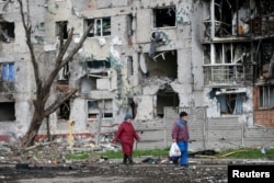 People walk near a residential building destroyed during Russia's assault on Ukraine, in the southeastern port city of Mariupol, April 22, 2022.