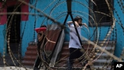 Dos niños caminan detrás de vallas de alambres de púas instaladas en el barrio San José del Pino, en Santa Tecla, El Salvador, en el marco de una campaña contra la violencia en la que fueron detenidos miles de presuntos pandilleros, el 6 de abril de 2022. 