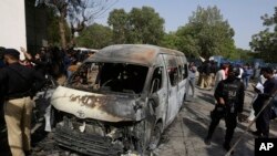 Pakistani investigators examine a burned van at the site of explosion in Karachi, April 26, 2022. 