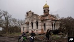 Residents walk with their bicycles in front of a damaged church, in Lukashivka, in northern Ukraine, April 22, 2022. Residents say Russian soldiers used the house of worship for storing ammunition, and Ukrainian forces shelled the building to make the Rus