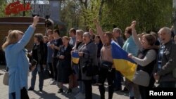 People shout slogans and hold Ukraine's national flag during a protest where tear gas was fired on them in Kherson, Ukraine, amid Russia's invasion of Ukraine, April 27, 2022 in this still image obtained from a social media video.