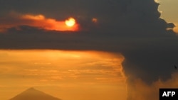 Matahari terbenam di balik Gunung Anak Krakatau (kanan) yang mengepulkan asap tebal, terlihat dari Pantai Pasauran, Anyer, Serang, 24 April 2022. (DZIKI OKTOMAULIYADI / AFP)