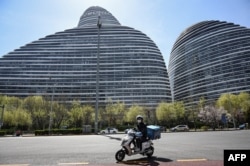北京一名快递工人骑着电动车路过一处发现了新冠感染者的办公楼。（2022年4月7日）