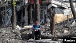 FILE - A man sits in a courtyard near a building damaged during the Ukraine-Russia conflict in the southern port city of Mariupol, Ukraine, April 25, 2022.