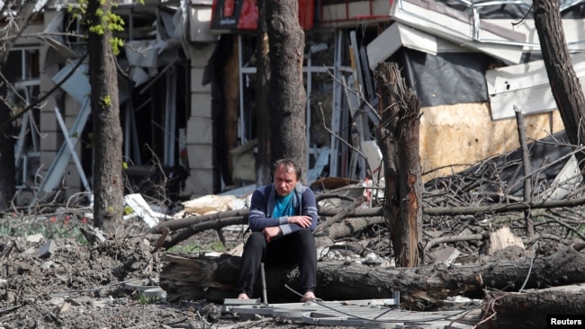 FILE - A man sits in a courtyard near a building damaged during the Ukraine-Russia conflict in the southern port city of Mariupol, Ukraine, April 25, 2022.