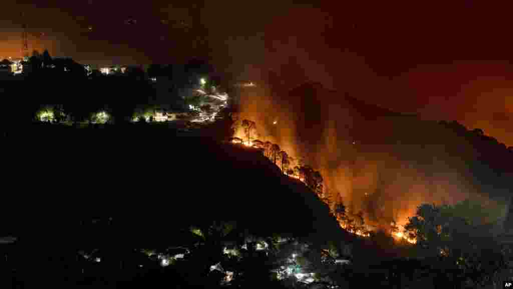 A forest on a mountain slope next to a township is seen on fire in Dharmsala, India, April. 25, 2022.