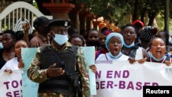 FILE - A policeman stands guard while members of the civil society chant slogans as they demonstrate against gender-based violence to mark International Women's Day in downtown Nairobi, Kenya, March 8, 2022. 