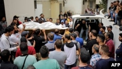 People gather at the entrance of the morgue of a hospital in Tripoli, as others carry the body of one of the people who died when their boat capsized a day earlier off the coast of the northern Lebanese city, April 24, 2022.