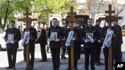 Men hold portraits of from left: Kira Glodan, three-month-old, her mother Valerya Glodan, 28, and grandmother Lyudmila Yavkina, 54, killed in their apartment by shelling, during a funeral ceremony at the Transfiguration Cathedral in Odesa, Ukraine, April 27. 2022.