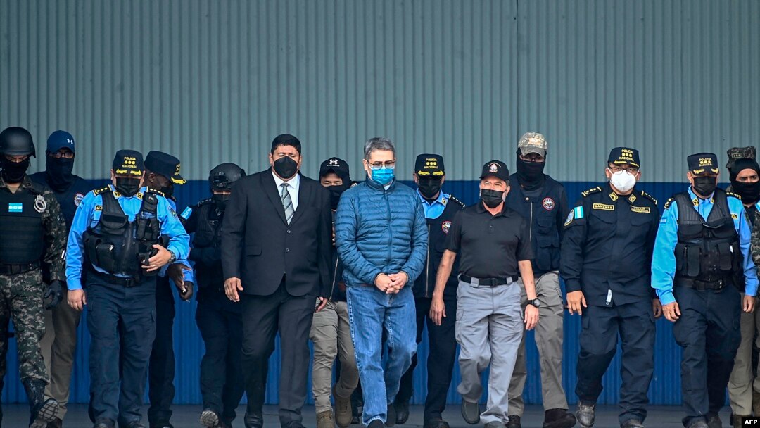 El expresidente hondureño Juan Orlando Hernández (C) es escoltado por el Ministro de Seguridad Ramón Sabillon y fuerzas de seguridad hacia un avión de la Agencia Antidrogas de Estados Unidos (DEA), durante su extradición a Estados Unidos el 21 de abril de 2022. 