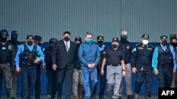 El expresidente hondureño Juan Orlando Hernández (C) es escoltado por el Ministro de Seguridad Ramón Sabillon y fuerzas de seguridad hacia un avión de la Agencia Antidrogas de Estados Unidos (DEA), durante su extradición a Estados Unidos el 21 de abril de 2022. 