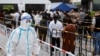 Seorang pekerja yang menggunakan APD berjalan di samping orang-orang yang mengantre untuk mengambil tes asam nukleat di tempat pengujian darurat COVID-19 di Beijing, China, 25 April 2022. (Foto: REUTERS/Carlos Garcia Rawlins)