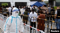 Seorang pekerja yang menggunakan APD berjalan di samping orang-orang yang mengantre untuk mengambil tes asam nukleat di tempat pengujian darurat COVID-19 di Beijing, China, 25 April 2022. (Foto: REUTERS/Carlos Garcia Rawlins)