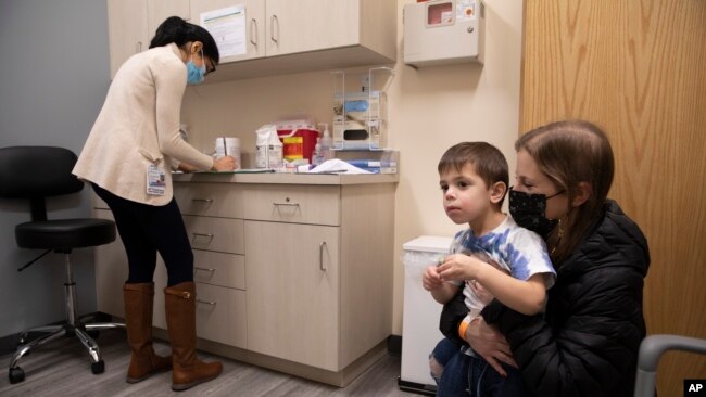 Ilana Diener memegang putranya, Hudson, 3, yang akan mengikuti uji coba pemberian vaksin COVID-19 Moderna di Commack, New York, pada 30 November 2021. (Foto: AP/Emma H. Tobin)