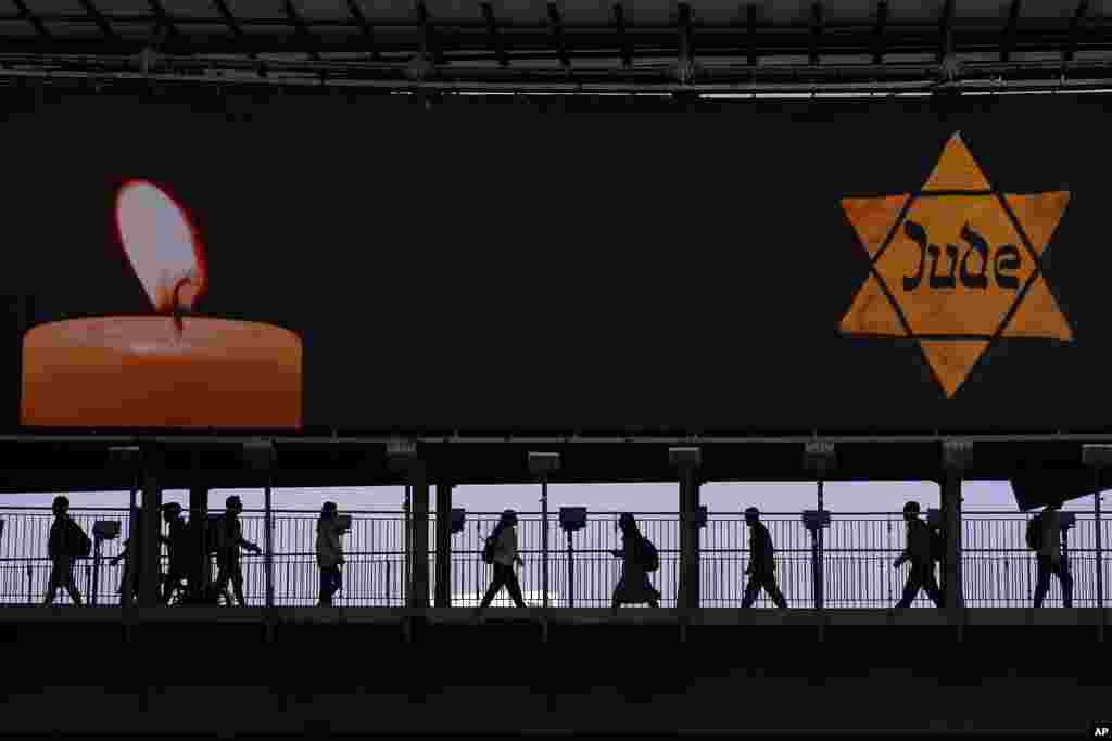 People walk along a bridge lit with a billboard showing a yellow Star of David that reads &quot;Jude,&quot; Jew in German, resembling the one Jews were forced to wear in Nazi Germany, during the yearly Holocaust Remembrance Day in Ramat Gan, Israel.