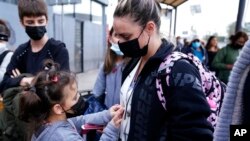 A woman from Ukraine stands with her children before crossing into the United States, March 10, 2022, in Tijuana, Mexico. U.S. authorities allowed the woman and her three children to seek asylum, a reversal from a day earlier when she was denied entry.