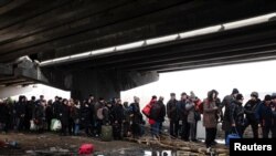 People flee under a destroyed bridge to cross the Irpin River as Russia's invasion on Ukraine continues, in Irpin outside Kyiv, Ukraine, March 9, 2022.