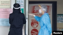 FILE - A health care worker wearing personal protective equipment (PPE) talks to a patient at a clinic designated to treat patients for COVID-19, in Hong Kong, China, March 7, 2022.