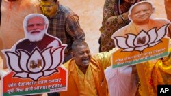 A Bharatiya Janata Party worker displays party symbol with photographs of Prime Minister Narendra Modi, left, and Uttar Pradesh Chief Minister Yogi Adityanath in Lucknow, India, March 10, 2022.