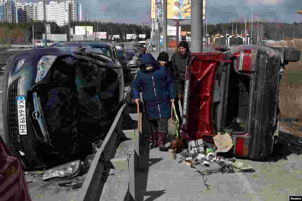 People walk between destroyed cars as they evacuate from Irpin, as Russia&#39;s attack on Ukraine continues, March 10, 2022.