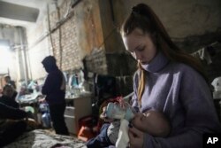 Seorang perempuan memberikan susu botol kepada bayi di sebuah tempat perlindungan bom sementara di Mariupol, Ukraina, 7 Maret 2022. (AP/Evgeniy Maloletka)