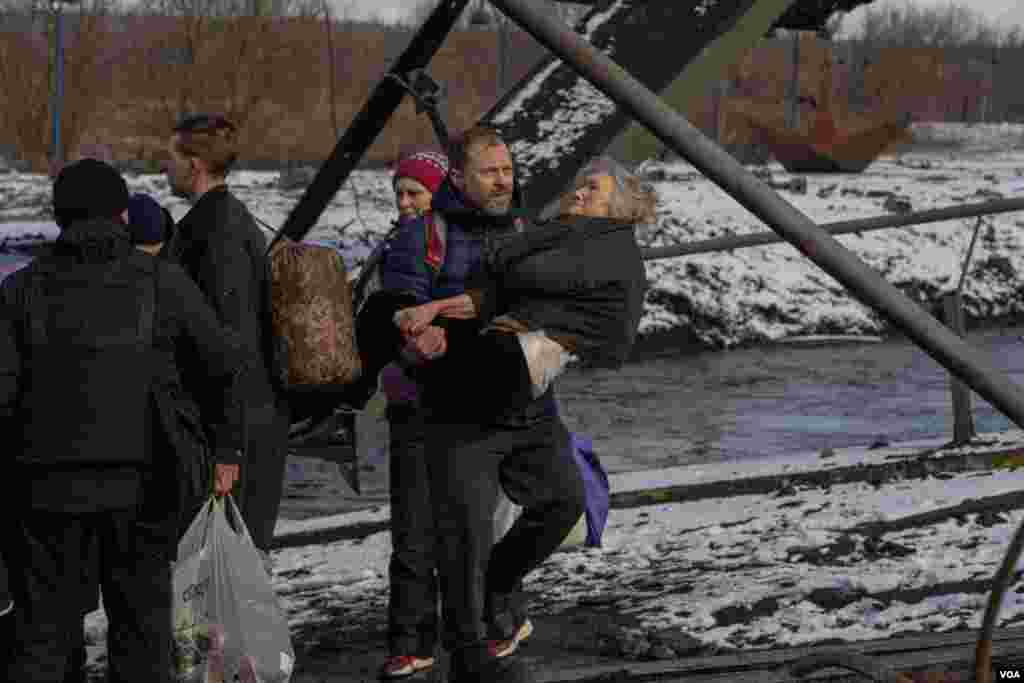 A man carries an elderly woman through an improvised path created under a bombed bridge over the Irpin River, in Ukraine, March 8, 2022. (Yan Boechat/VOA) 