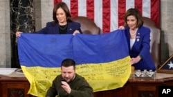 Vice President Kamala Harris and House Speaker Nancy Pelosi of Calif., right, hold a Ukrainian flag autographed by front-line troops in Bakhmut that Ukrainian President Volodymyr Zelenskyy presented to lawmakers in Washington, Wednesday, Dec. 21, 2022. (AP Photo/Carolyn Kaster)