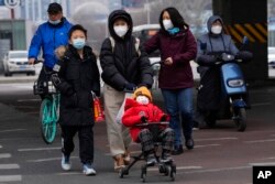 A child wearing a mask is pushed across a road in Beijing, Dec. 2, 2022.