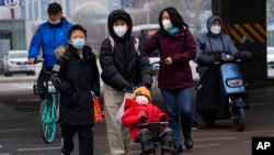 A child wearing a mask is pushed across a road in Beijing, Dec. 2, 2022. 