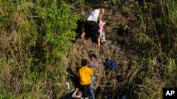 A Venezuelan migrant grips a child as he climbs a river bank onto U.S territory, after crossing from Matamoros, Mexico, Dec. 22, 2022.