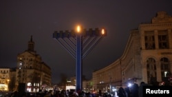 Warga berdiri di dekat sebuah menorah raksasa dalam perayaan Hanukkah di alun-alun Kota Kyiv, Ukraina, pada 18 Desember 2022. (Foto: Reuters/Valentyn Ogirenko)