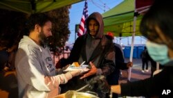 Seorang pengungsi (tengah) menerima makanan dari para relawan yang berada di luar Gereja Sacred Heart di El Paso, Texas, pada 7 Januari 2023. (Foto: AP/Andres Leighton)