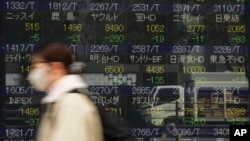 Seorang perempuan berjalan melewati monitor yang menunjukkan harga pasar saham perusahaan Jepang di sebuah perusahaan sekuritas di Tokyo, Jumat, 2 Desember 2022. (AP/Hiro Komae)