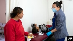 Dr. Krystal Lopez, right, with the Texas Tech University Health Sciences Center in El Paso, Texas, provides medical attention to a 5-year-old Honduran migrant as his mother looks on at a government-run shelter in Ciudad Juarez, Mexico, Dec. 18, 2022.