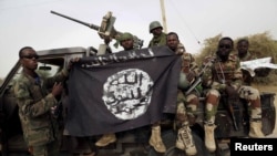 FILE - Nigerian soldiers hold up a Boko Haram flag that they seized after retaking the town of Damasak, Nigeria, March 18, 2015.