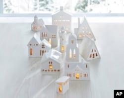 This image provided by Crate & Barrel shows their collection of white ceramic buildings. Crate & Barrel's collection includes alpine homes and hotels as well as midcentury split levels and ranch homes. Add a tealight for a welcoming glow. (Crate & Barrel via AP)